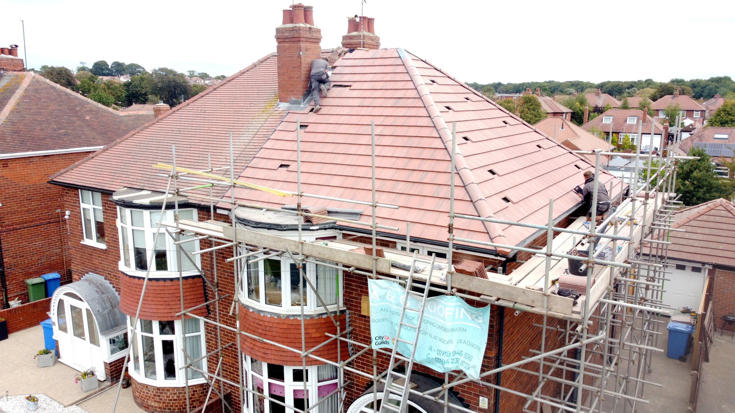 A & G Roofing fitting a new tiled roof on a semi-detached house, with the scaffolding up and their banner on it