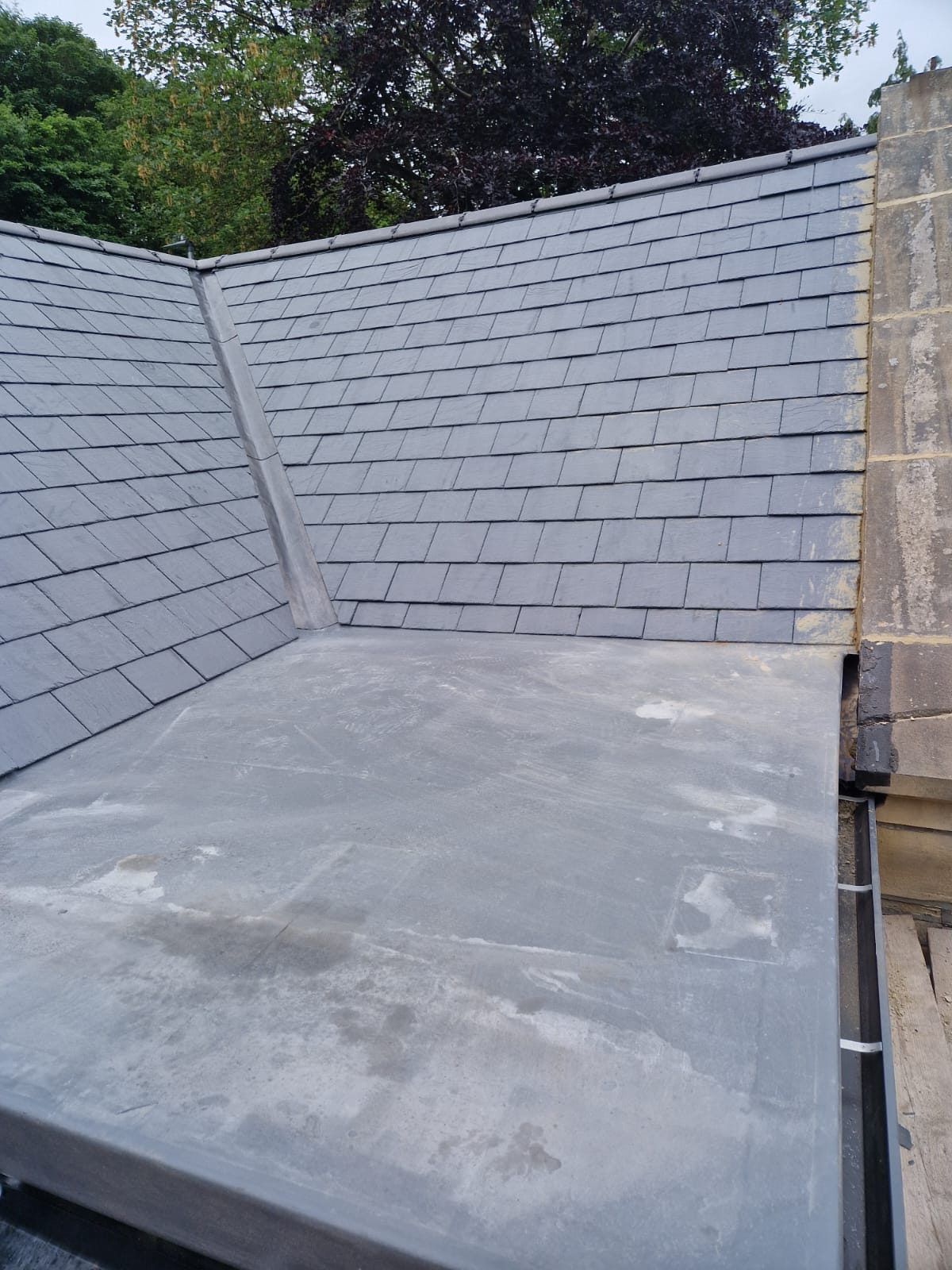 Grey flat roof between two slate roof slopes