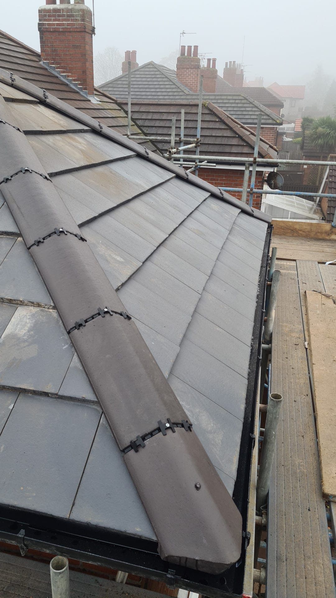 Grey tiled roof with a new dry ridge, scaffolding below
