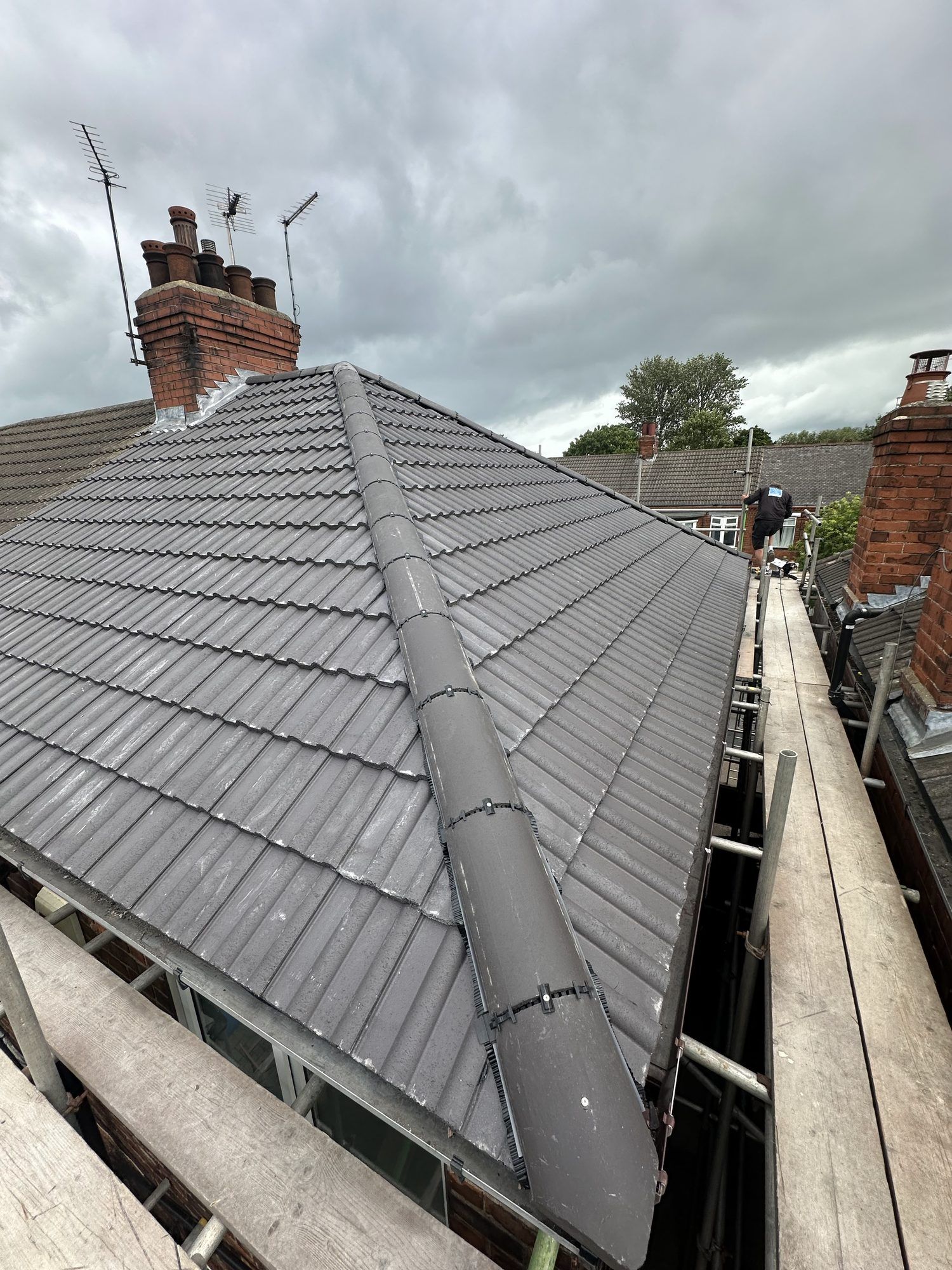 Grey tiled hip roof with a dry ridge, brick chimney stacks behind
