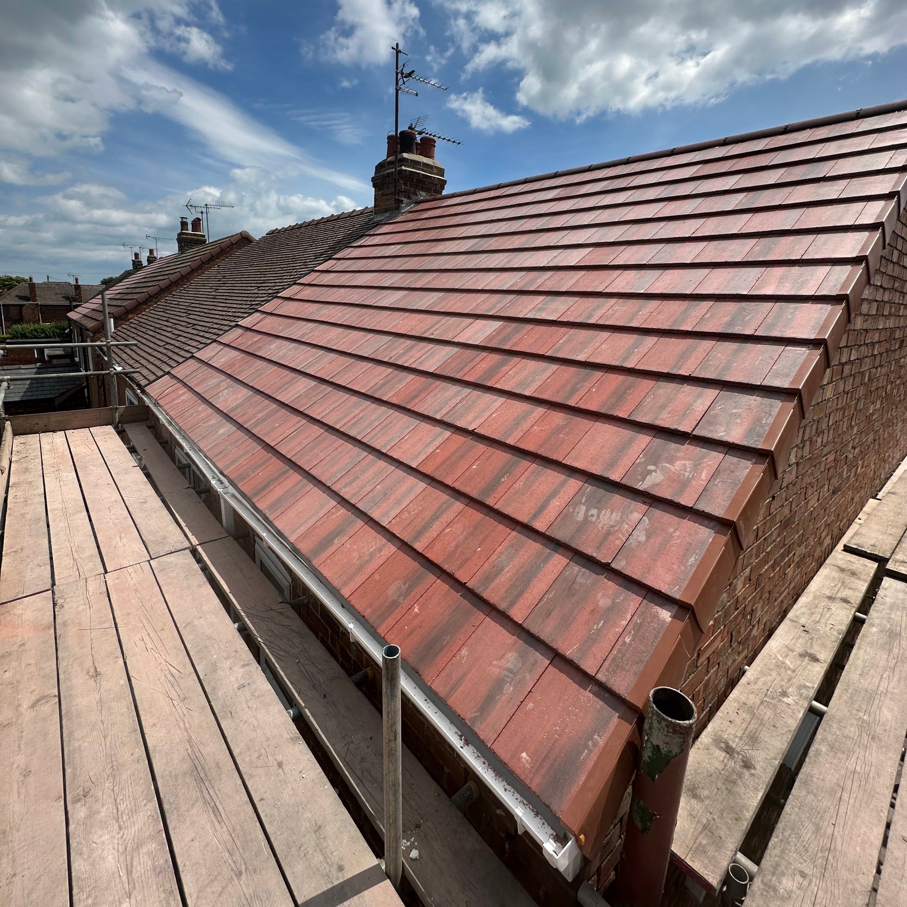 A new red-brown tiled roof with a brick chimney, under a blue sky with white clouds