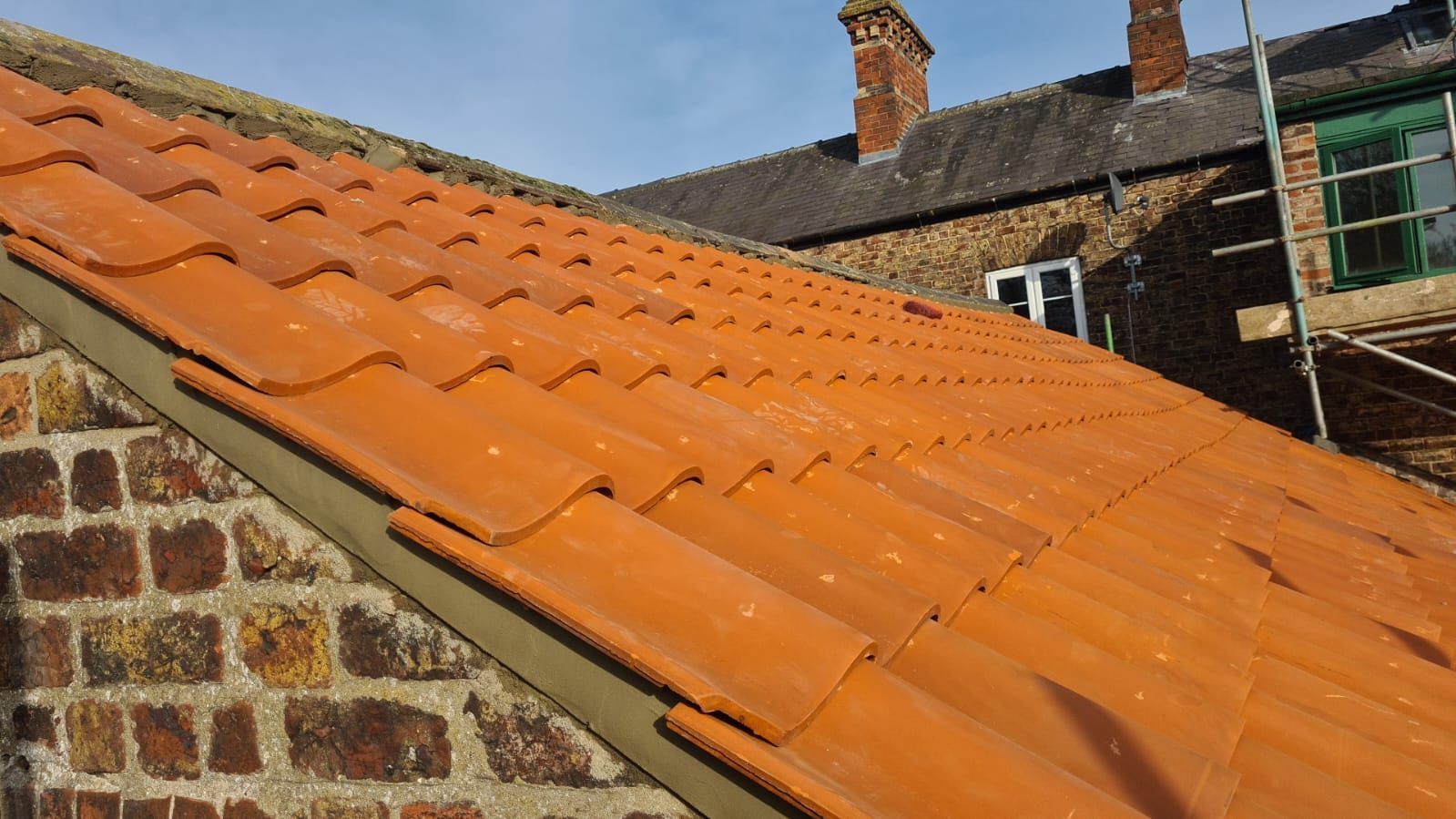 Orange clay pantiles along the edge of a brick house roof