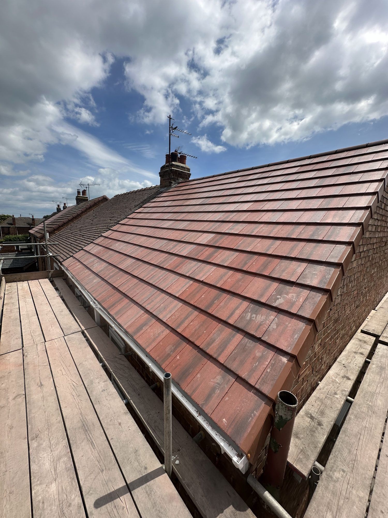 New red-brown tiled roof under a big cloudy sky, seen from the scaffold