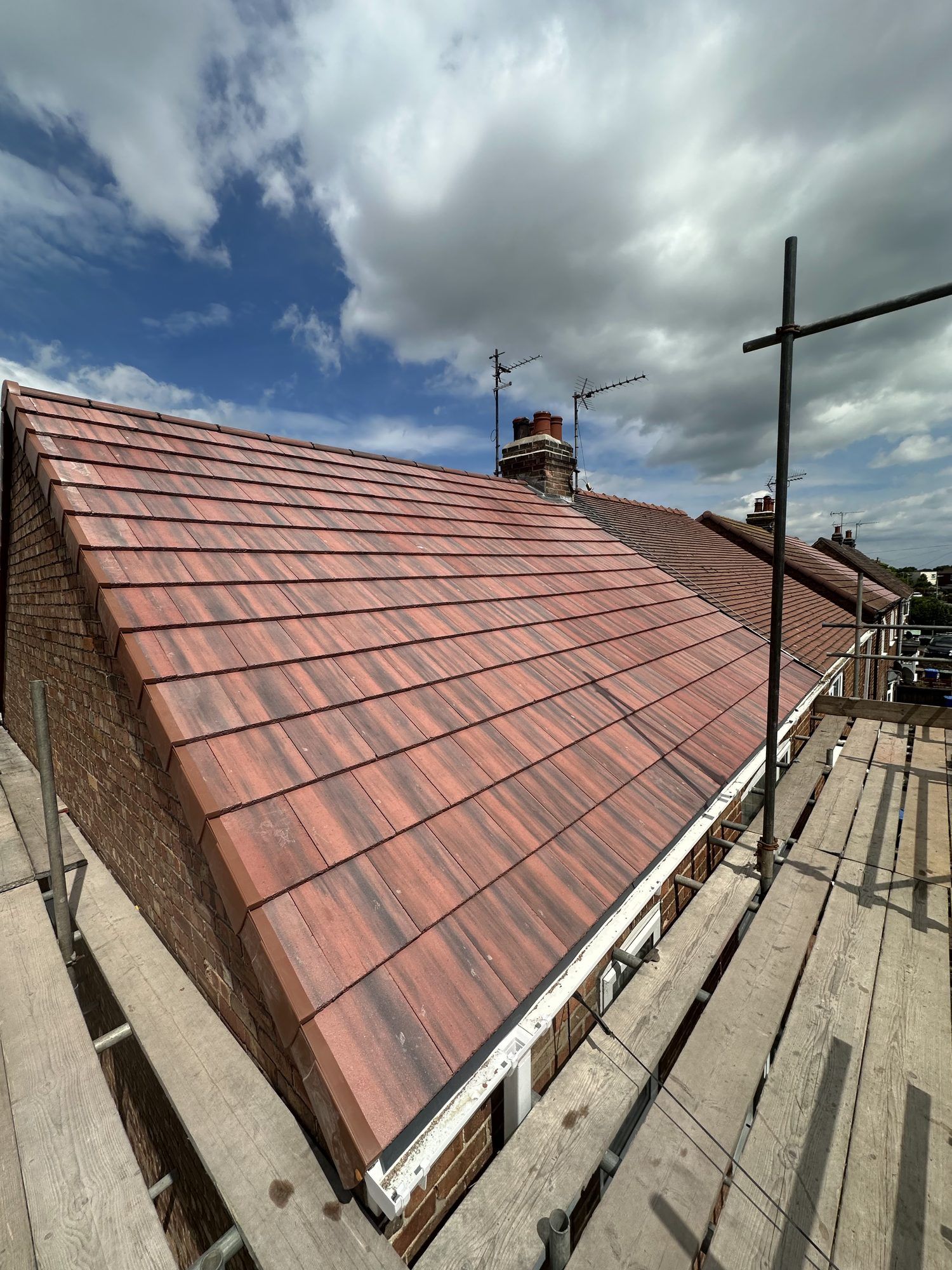 Red-brown tiled roof under a cloudy sky, with scaffolding along the eaves