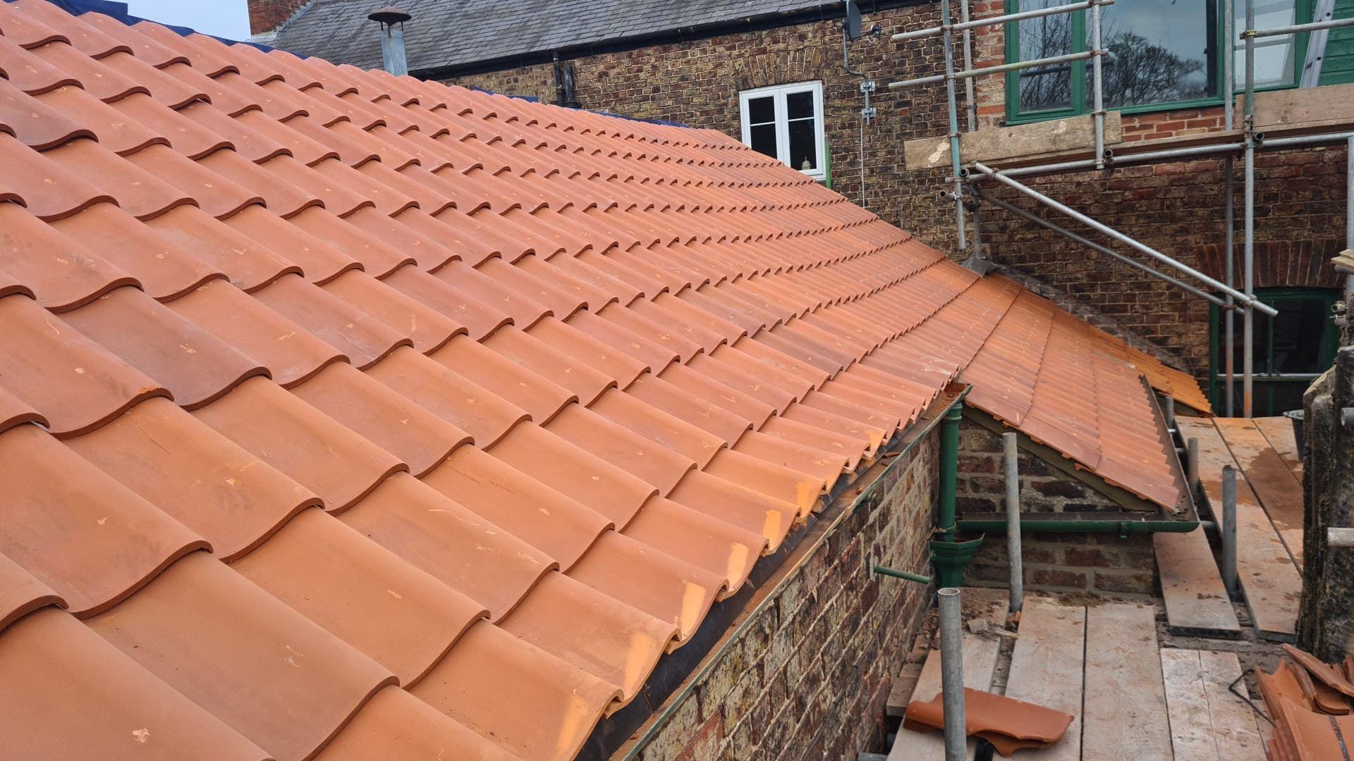 New red interlocking tiles on a brick house, with scaffolding