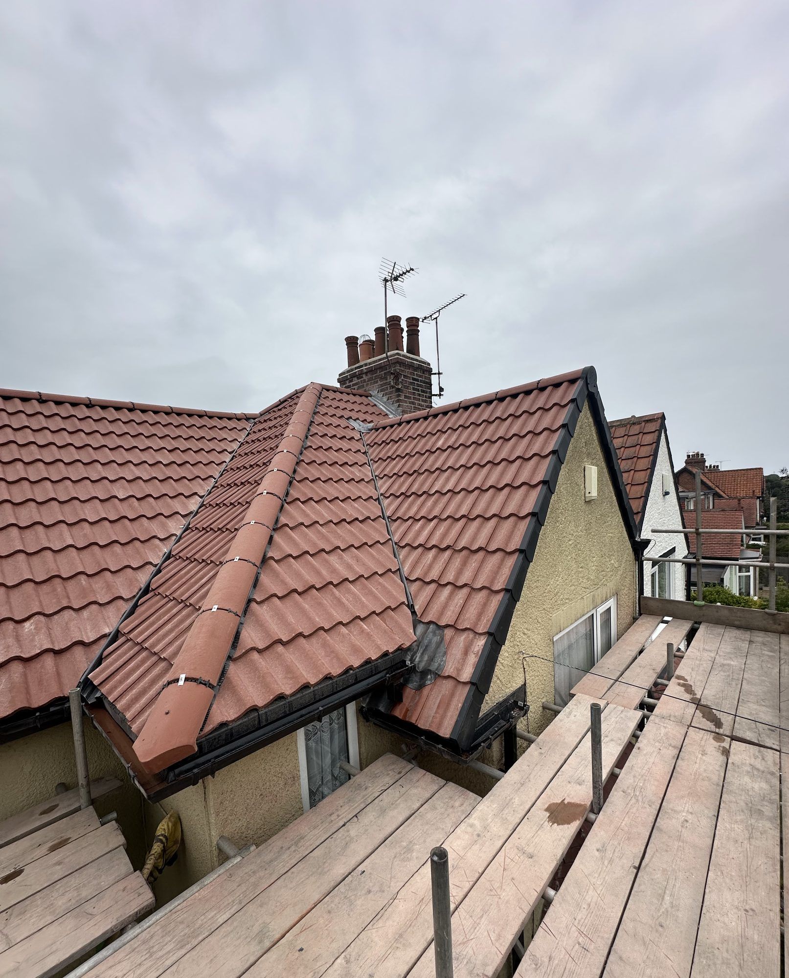 Red tiled roof with a new dry ridge on a hip, beside a rendered wall