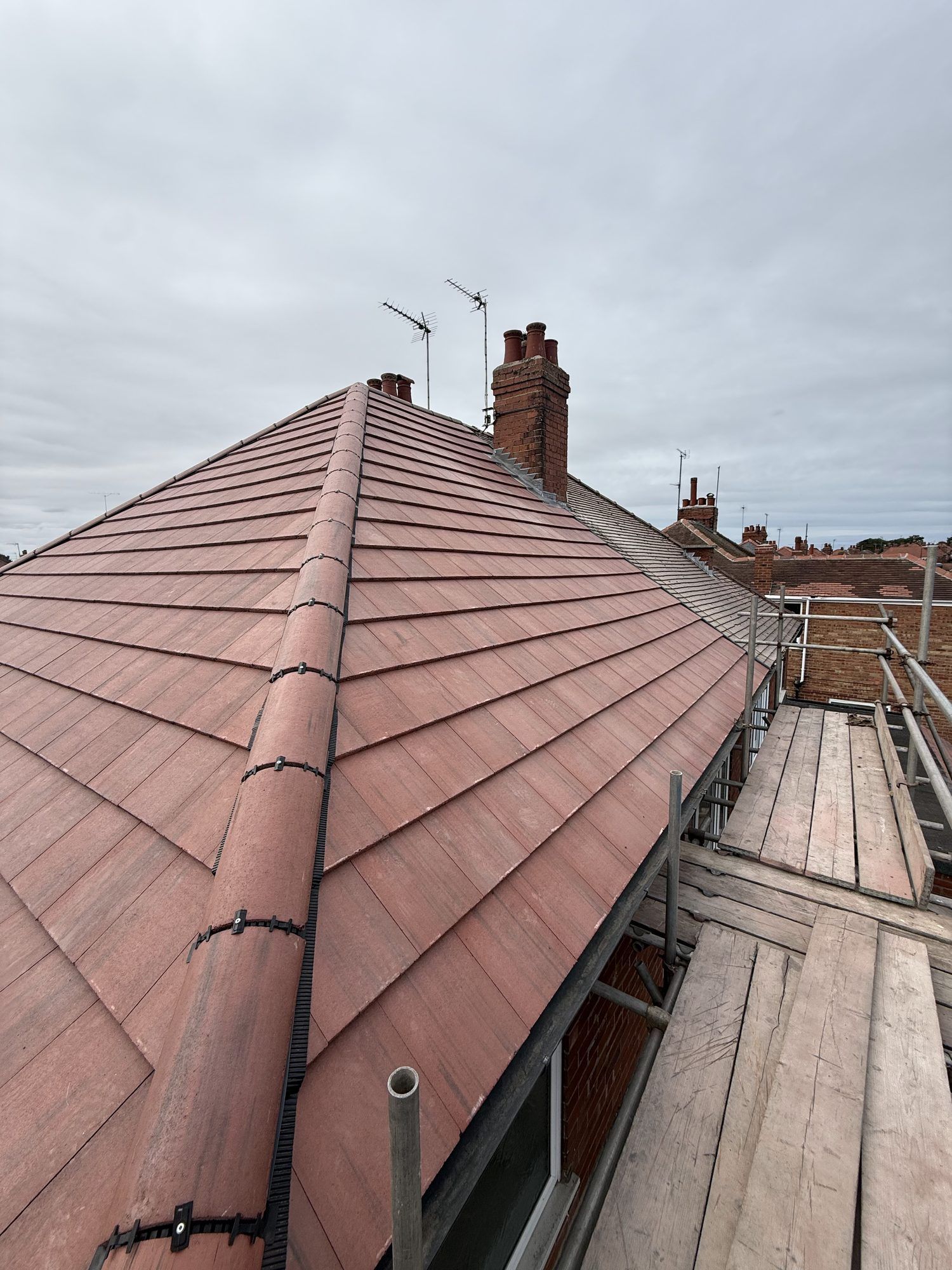 New red tiled hip roof with a dry hip ridge, seen from the scaffold