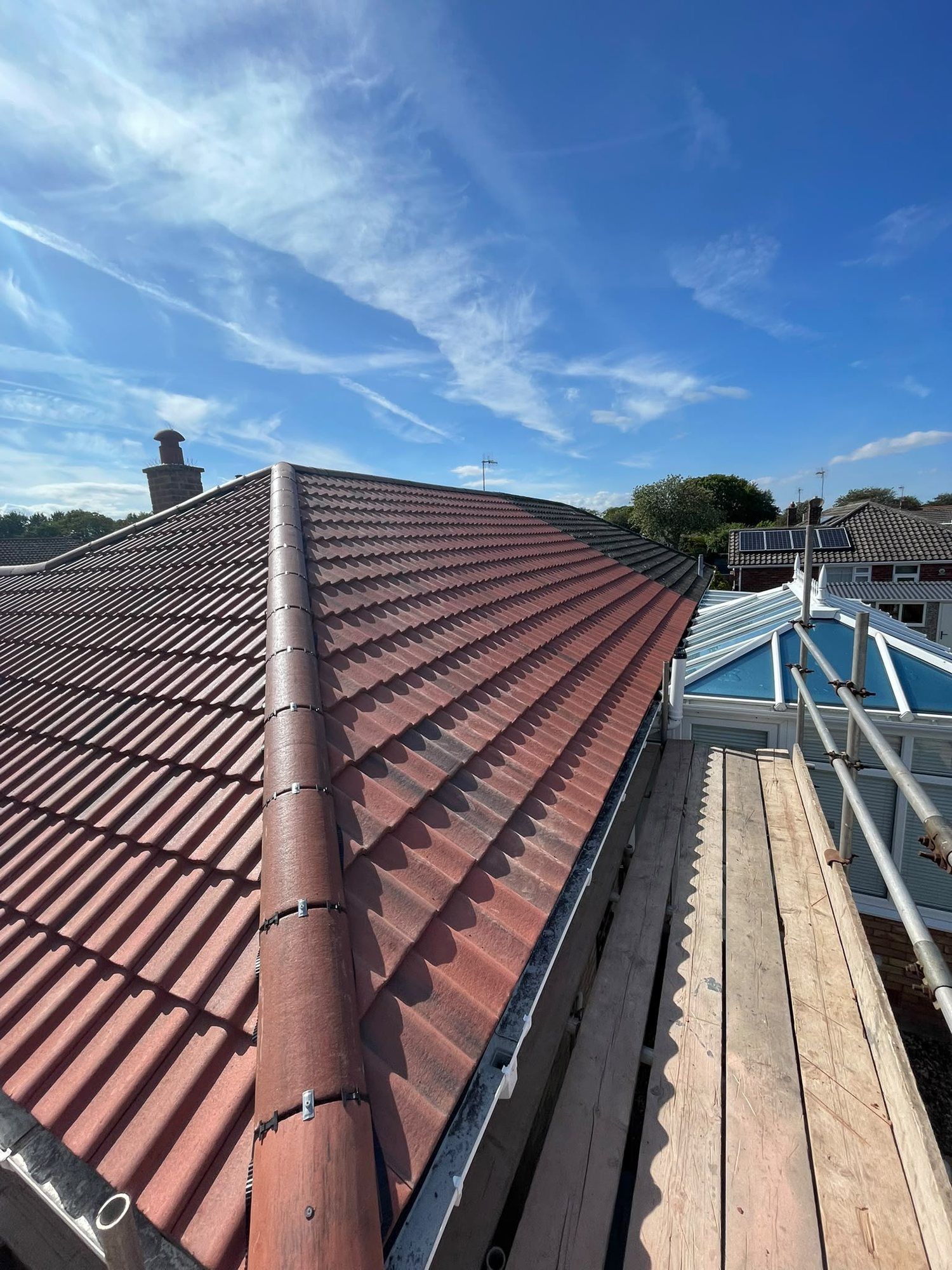 New red tiled roof with a dry ridge under a blue sky, a conservatory below