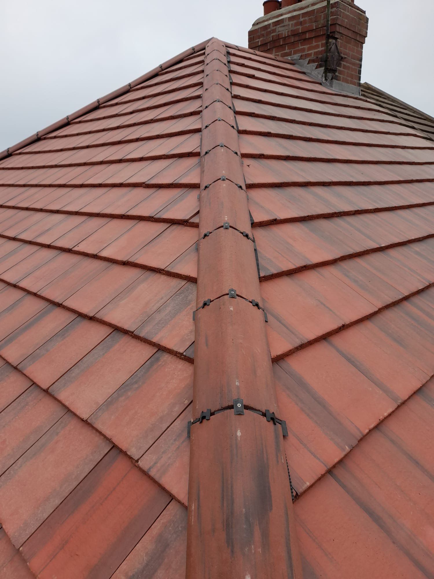 Red tiled roof running up to its ridge, with a brick chimney