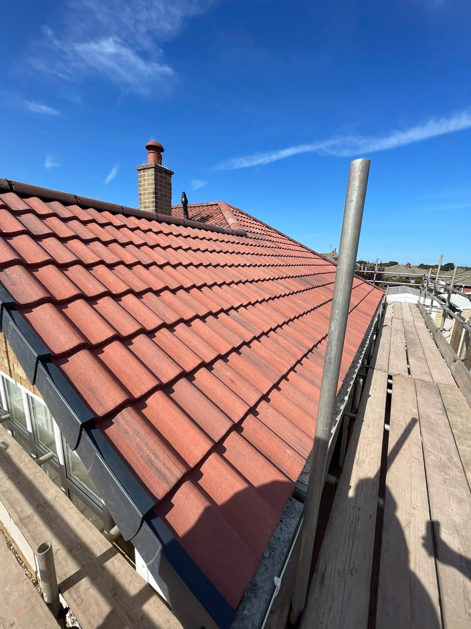 Red interlocking tiles with dark fascias, a chimney beyond, seen from the scaffold