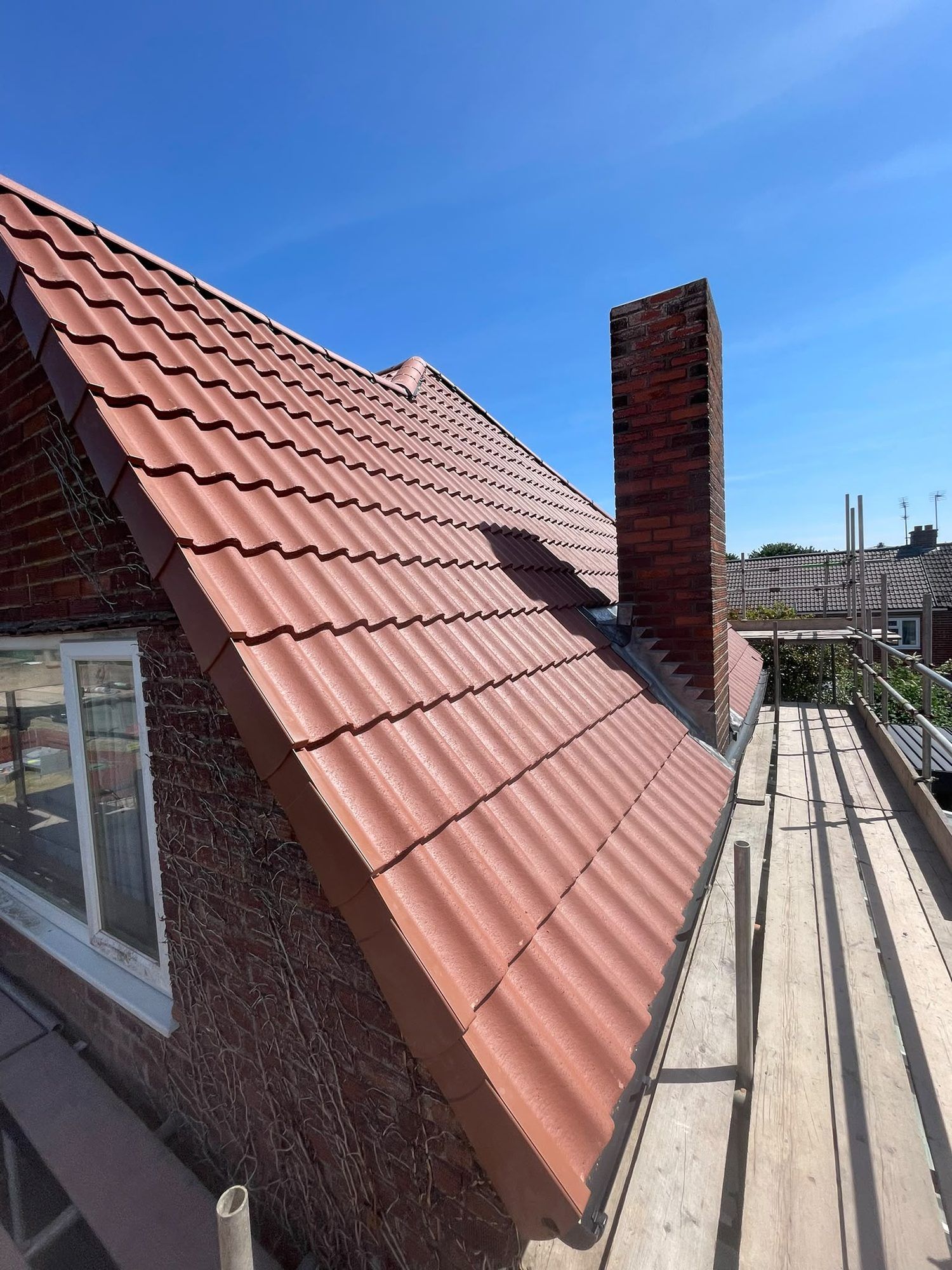 New red tiled roof and brick chimney against a blue sky