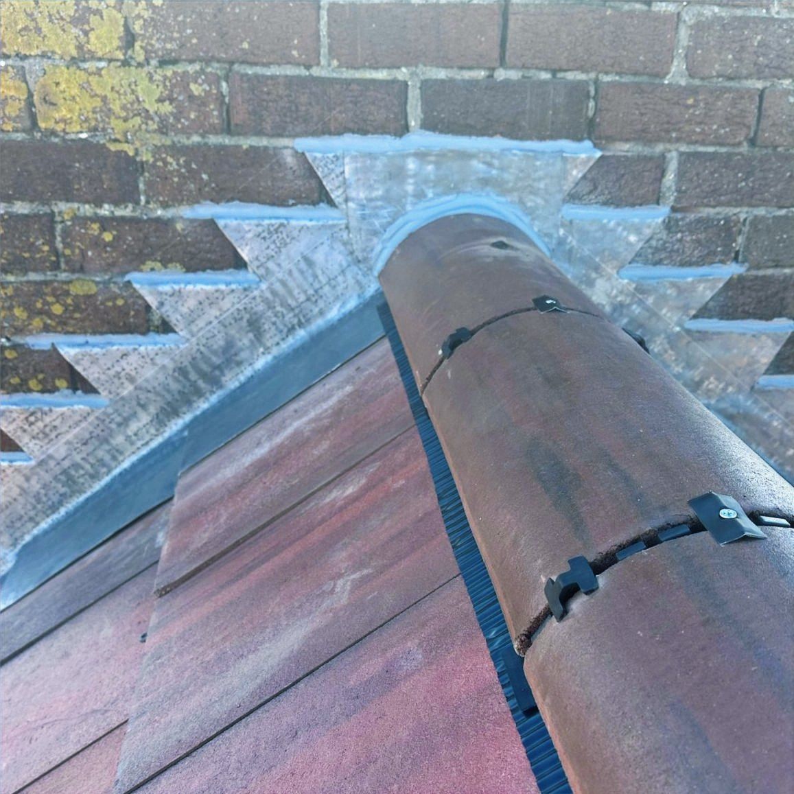 Red ridge tiles meeting a brick wall, sealed with new lead flashing