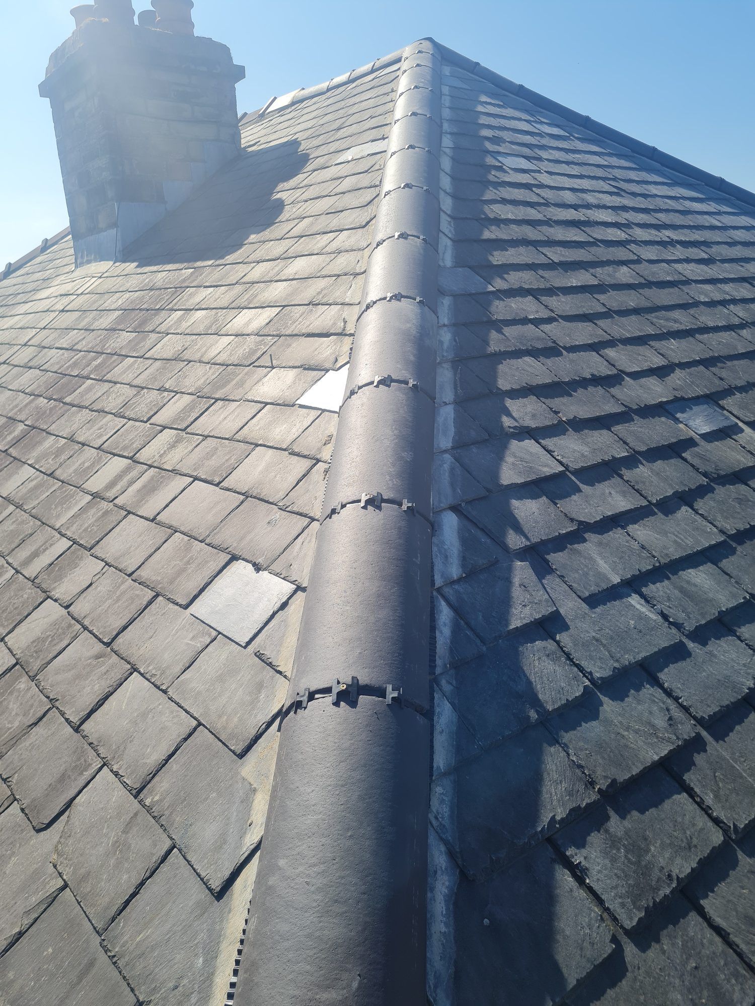 Slate roof with a new dry ridge running up to a chimney stack